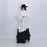ホワイトのロングシャツ 着用 帽子を押さえたポーズ